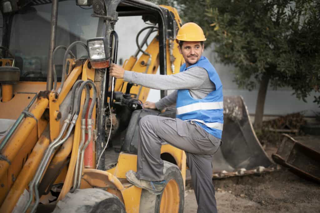 Construction worker climbing a backhoe