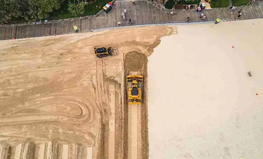 Aerial view of bulldozers shaping a beach near a boardwalk